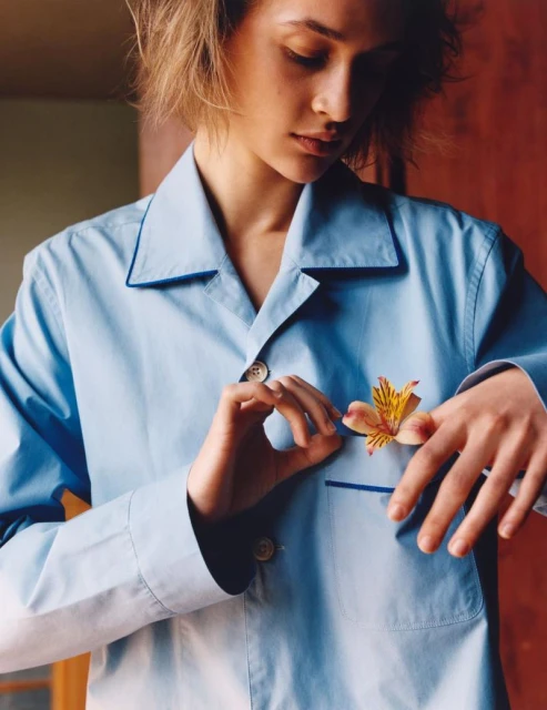 Young woman wearing a blue pajama shirt and holding a yellow flower. The photo is a close-up shot with indoor lighting and background.