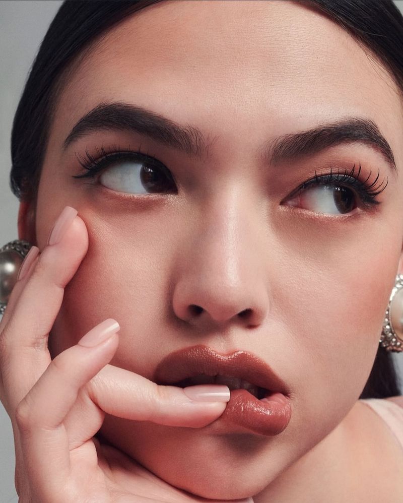 Portrait of an Asian woman with finger on lips, wearing pearl earrings, looking up and away.  Beauty and makeup concept.