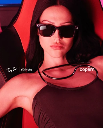 Indoor shot of a stylish adult female wearing sunglasses and a black dress, seated in a red and black gaming chair against a blue screen.