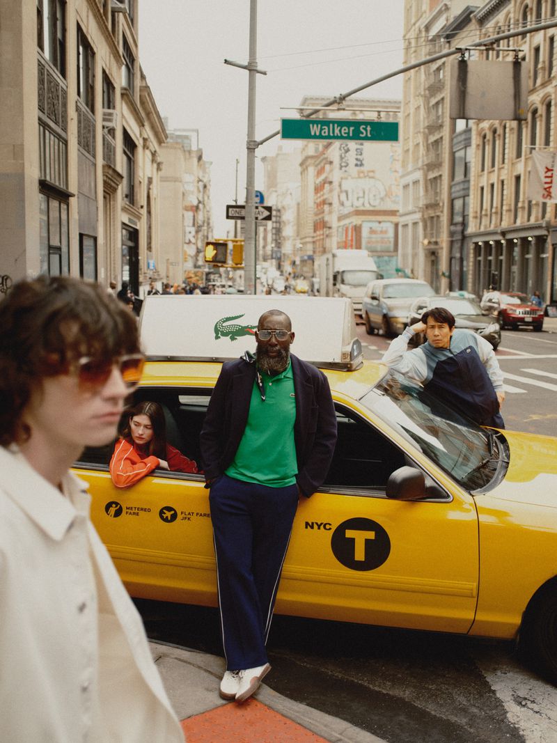 Four people stand on a city street next to a yellow taxi cab. An adult male leans against the cab, with an adult female and two other adults nearby.