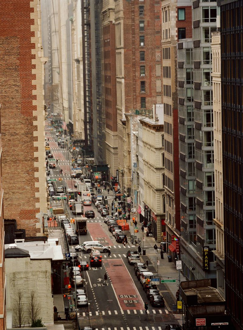 High angle view of New York City street featuring traffic, pedestrians, and tall buildings, with a brick building on the left.