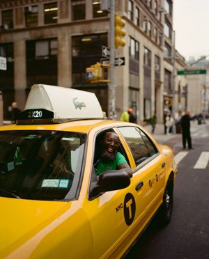 Man with beard smiling from inside a yellow New York City taxi cab wearing a green polo shirt