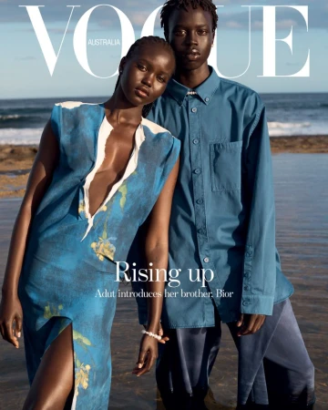 Magazine cover featuring two models on a beach. Vogue Australia cover with a man and a woman in blue clothing standing in the ocean.