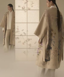 Model wearing embroidered floral coat standing beside a lighted shoji screen panel in a campaign by Yuriko Takagi for Dior.