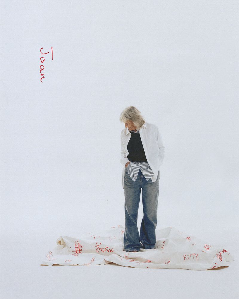 Woman in casual clothes stands on a cloth with red writing in a brightly lit studio setting. Fashion editorial photography.