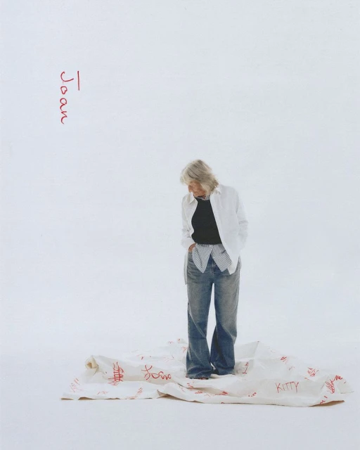 Woman in casual clothes stands on a cloth with red writing in a brightly lit studio setting. Fashion editorial photography.