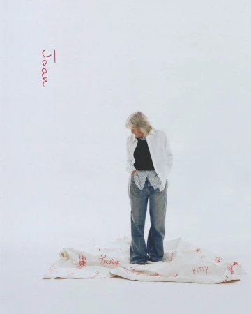 Woman in casual clothes stands on a cloth with red writing in a brightly lit studio setting. Fashion editorial photography.