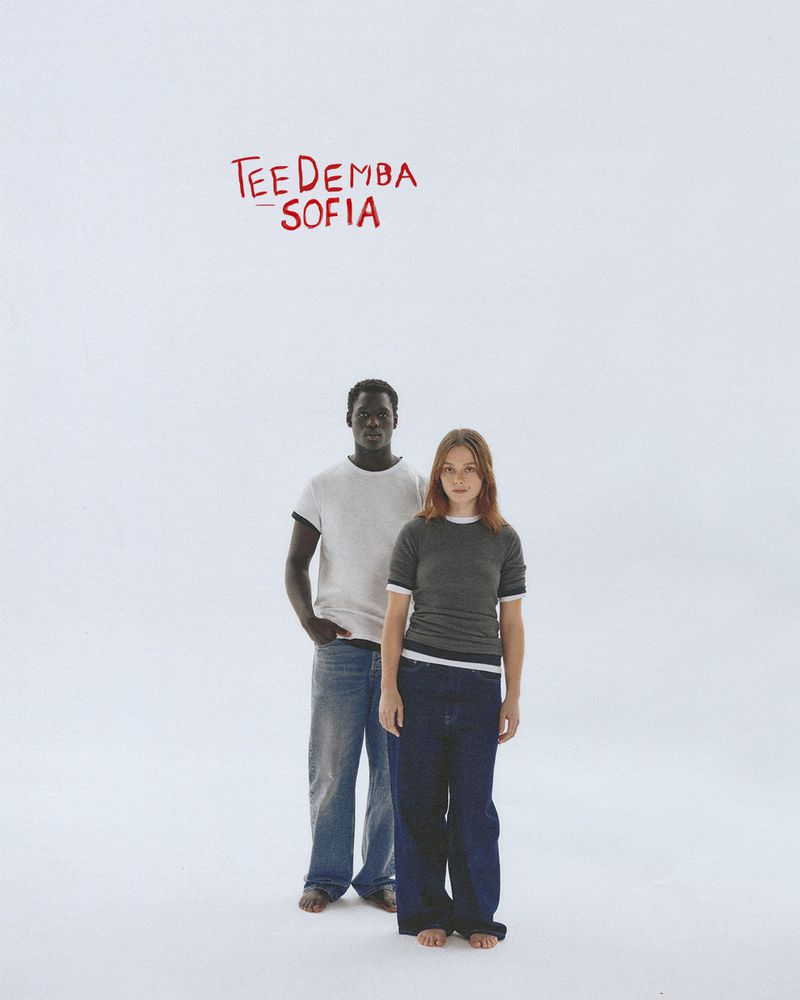 A man and a woman pose in front of a white background with red typography above them. The models wear casual clothing and stand barefoot.