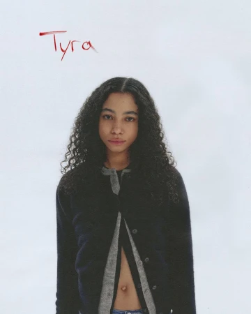 Young woman with long curly dark hair wearing a dark cardigan against a white background