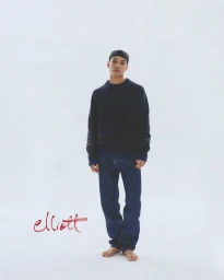 Man wearing a dark blue crewneck sweater and jeans standing against a plain white background with red script text.
