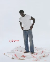 Man in white ringer t-shirt and blue jeans standing on a sheet covered in red handwritten text against white background