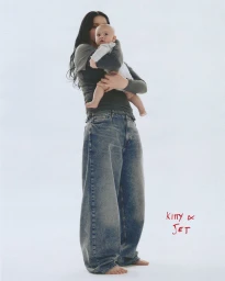 Woman with long dark hair holding an infant baby against a plain white background