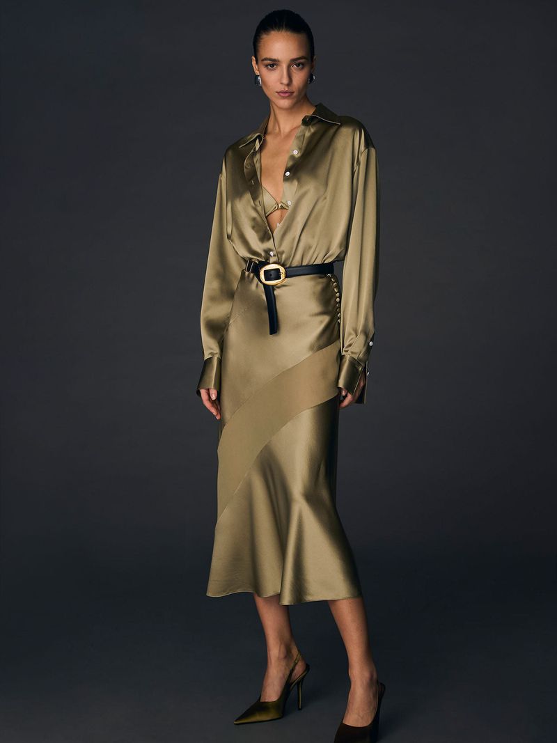 Fashionable adult woman in silk blouse and skirt with black belt stands in a studio with a dark background, posing for a fashion shot.