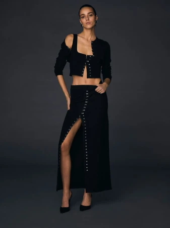 Model Emm Arruda wearing black coordinated separates with metal closures against dark background.