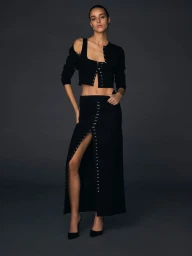 Model Emm Arruda wearing black coordinated separates with metal closures against dark background.