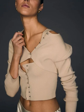 Model Emm Arruda wearing a beige knit cardigan by designer Joseph Altuzarra for Victoria's Secret against a dark grey background.