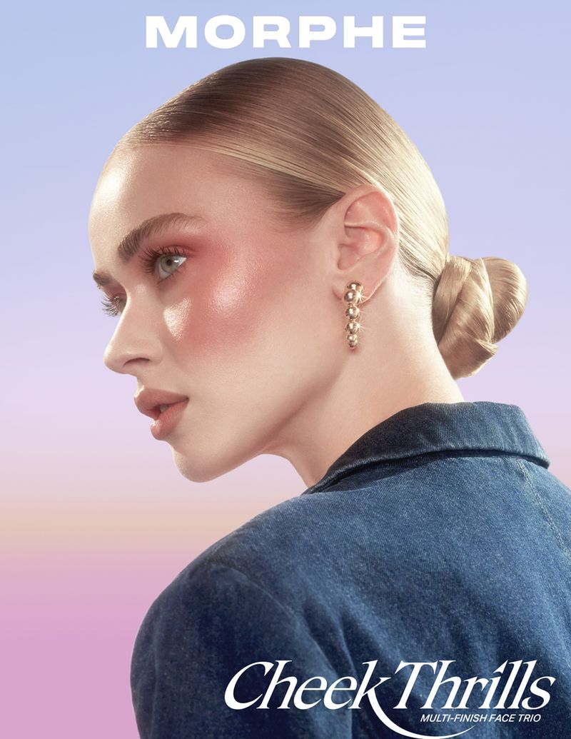Blonde woman with pink blush and a blue jacket poses in front of a gradient background, promoting Morphe Cheek Thrills makeup.